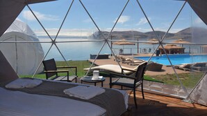 A tented accommodation with a bed, chairs, and a view of a swimming pool and mountains. - Comuna Sevan beach Glampings (Artanish)