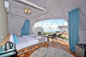 Una carpa amplia con cama, mesa, sillas y vistas del paisaje.