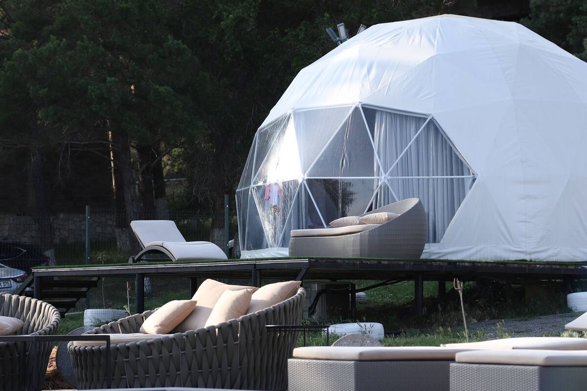 A dome-shaped tent with a white exterior and a transparent section, surrounded by lounge chairs and a swimming pool.