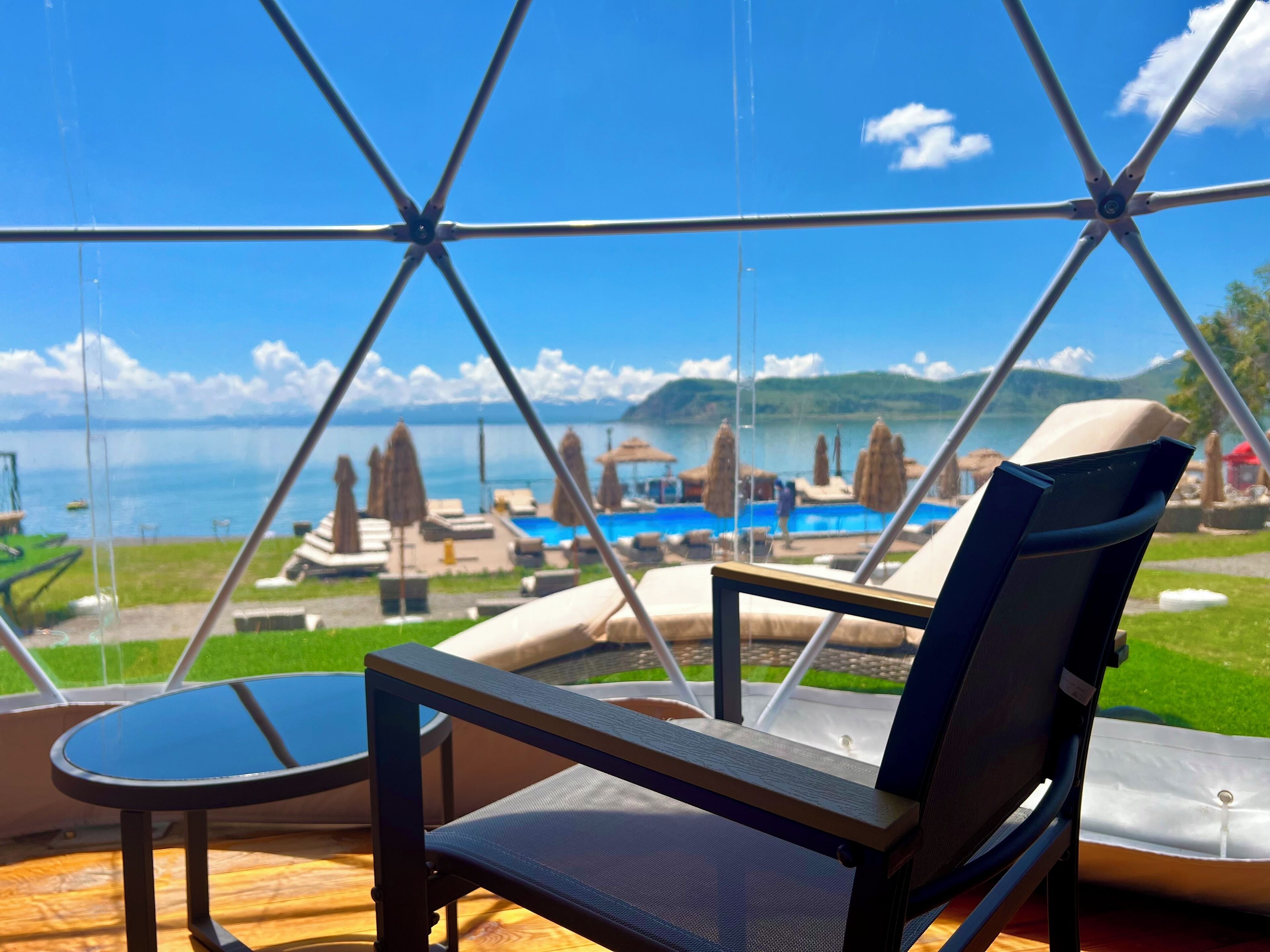 A glass-enclosed room with a view of a pool and lounge chairs.