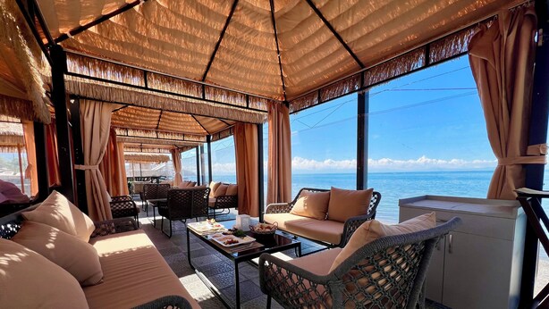 A sunlit lounge area with wicker furniture, a coffee table, and a view of the sea. - Comuna Sevan beach Glampings (Artanish)