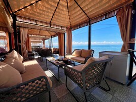 Un área de descanso soleada con muebles de mimbre, una mesita de café y vista al mar.