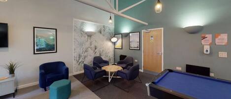 A pool table, four chairs, a small table, and a plant in a room with a blue and white color scheme.