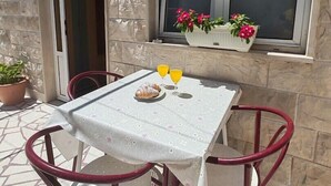 An outdoor patio with a table set for two, a potted plant, and a window with flowers. - Apartments Lucerna / Comfort 3 apartment for 4 people (Neum)