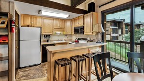 Une cuisine avec des meubles en bois, un réfrigérateur blanc, une cuisinière et une grande fenêtre donnant sur un quartier résidentiel.