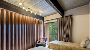 Une chambre avec deux lits, un mur recouvert de lambris en bois, une chaise avec un coussin et une fenêtre avec des rideaux.