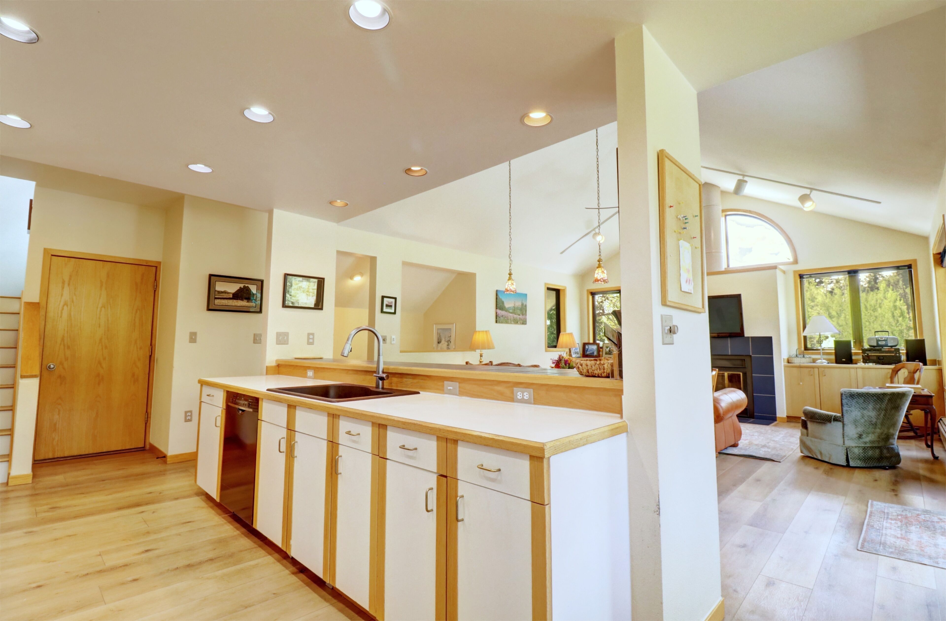 A spacious kitchen with wooden cabinets, a built-in dishwasher, and a large island with a sink. There is a dining area with a sofa and a chair, and a fireplace in the background.