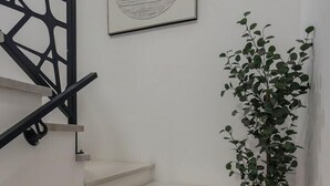 Una escalera con barandilla geométrica, una obra de arte en un marco en la pared, y una planta en maceta.