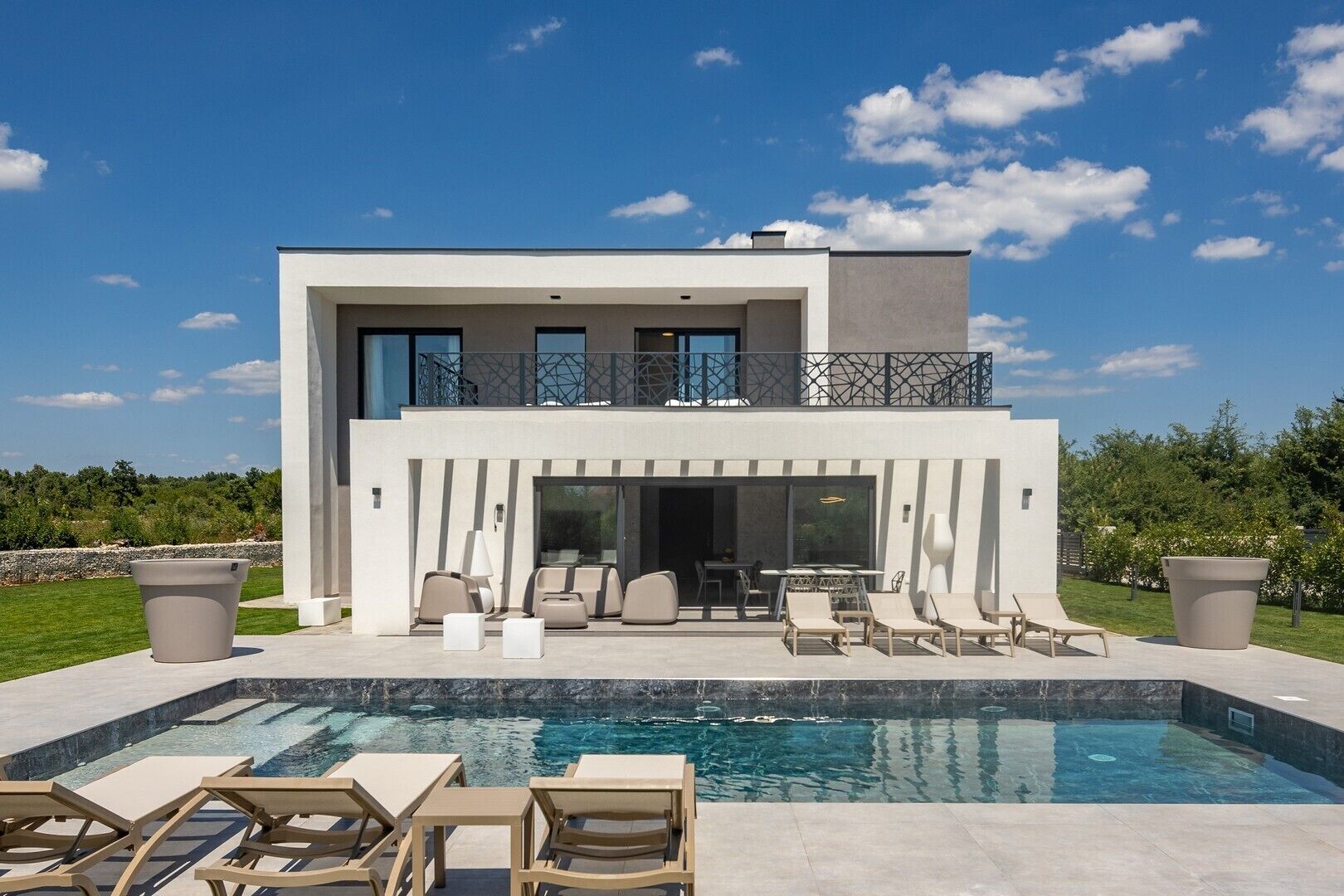 A modern two-story house with a pool, outdoor seating, and a balcony.
