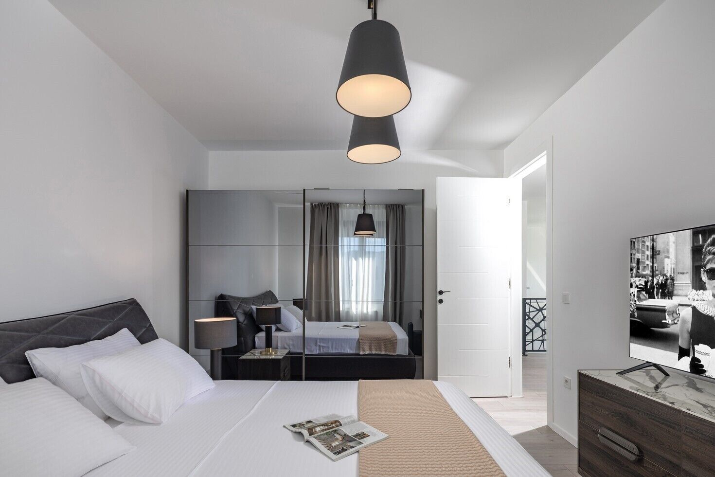 Una habitación de hotel moderna con una cama grande, una mesita de noche, un espejo y un televisor.