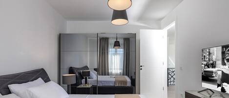 Una habitación de hotel moderna con una cama grande, una mesita de noche, un espejo y un televisor.