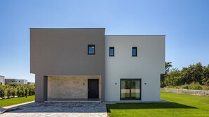 Una casa moderna de dos pisos con techo plano, un acceso principal amplio y dos ventanas pequeñas en el nivel superior.