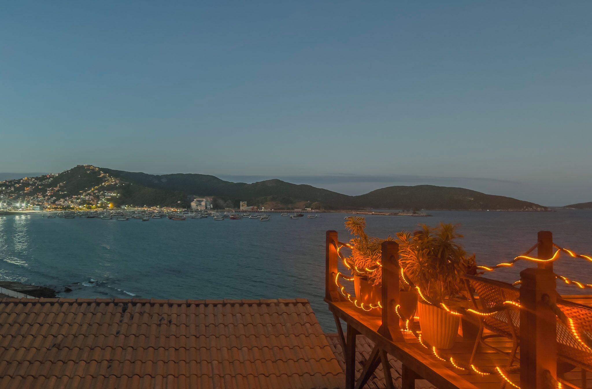 A coastal view with a terrace overlooking the sea, featuring a table with potted plants and string lights.