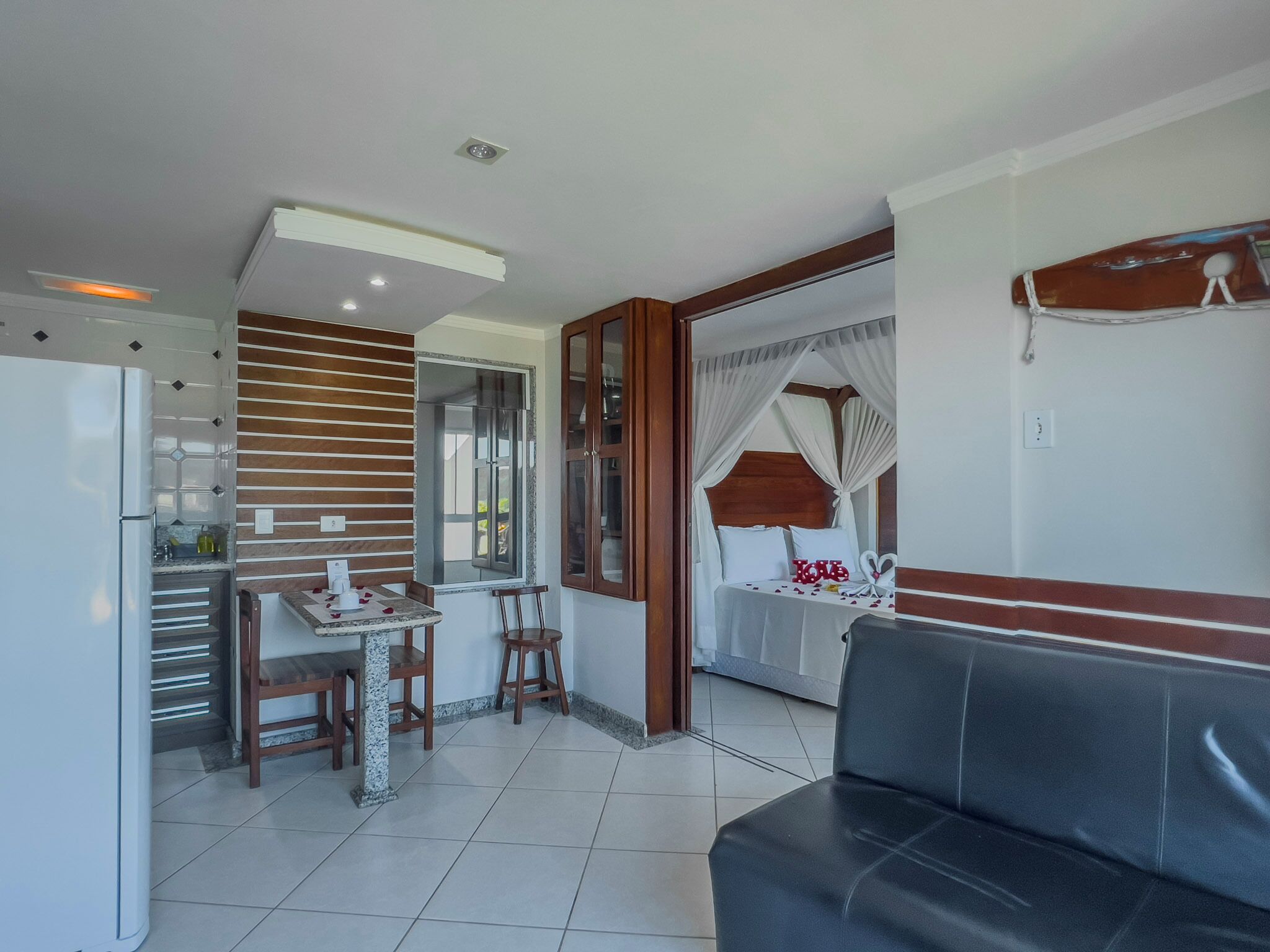A modern kitchen with a refrigerator, wooden panel wall, and a dining area with a table and chairs.