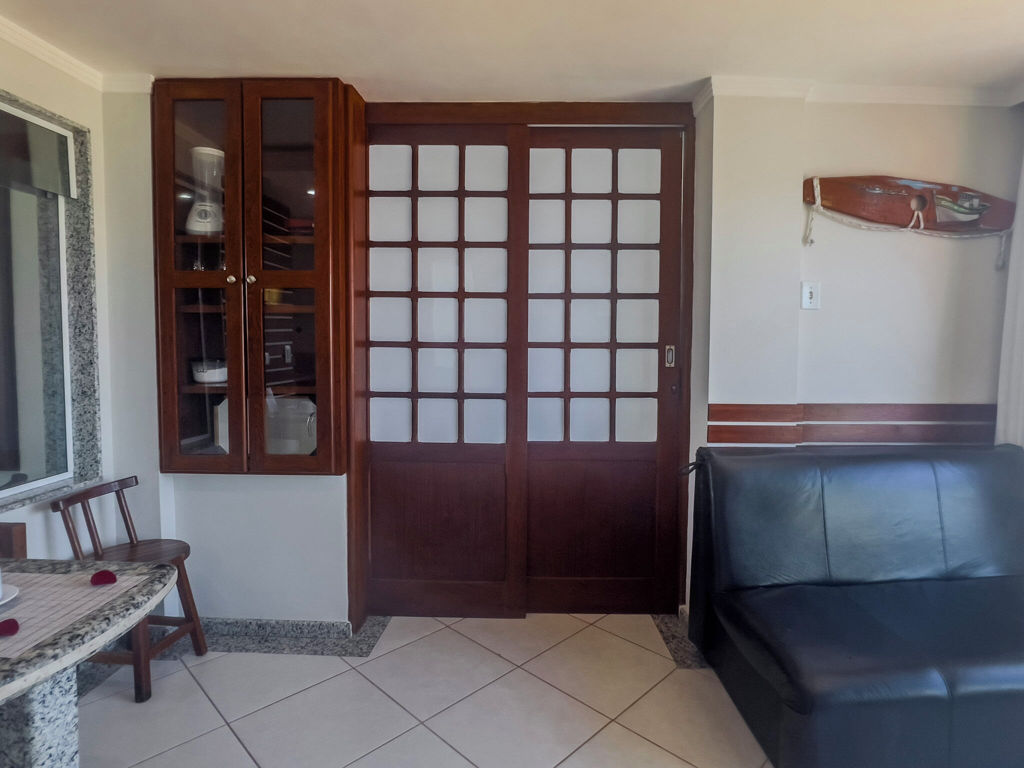 A room with a dining table, chairs, a black leather sofa, a wooden cabinet with glass doors, and a decorative wall piece.