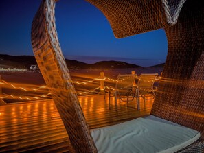 A beachside lounge with wicker furniture and a view of the ocean at dusk. - Luxo e Praia Exclusiva para Casal (Arraial do Cabo)