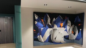 Un intérieur moderne avec un grand tableau abstrait au mur, un banc en bois et une porte portant l’inscription « LOCATION DE SKIS ».