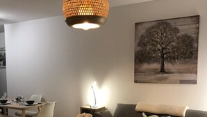 Un salon moderne avec un canapé gris, une table à manger avec des chaises, un luminaire suspendu et un tableau représentant un arbre accroché au mur.