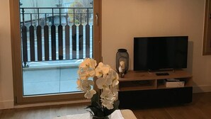 Un salon avec une télévision, un miroir rond et un vase rempli de fleurs blanches, posé sur une table.