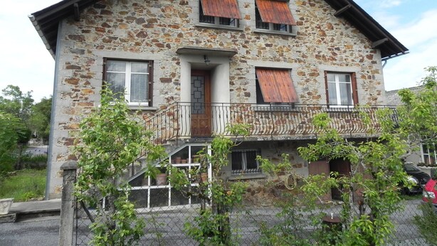 A stone house with a balcony, a wooden door, and a window with shutters. - Location Saisonnière Aveyron (Sauveterre-de-Rouergue)