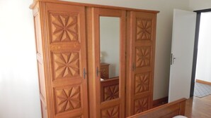 A bedroom with a wooden wardrobe, a bed, and a mirror. - Location Saisonnière Aveyron (Sauveterre-de-Rouergue)