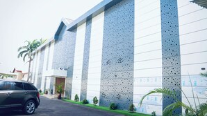A modern building with a large perforated facade, a parking area, and a few potted plants. - Grand Palmac Hotel (Abuja)