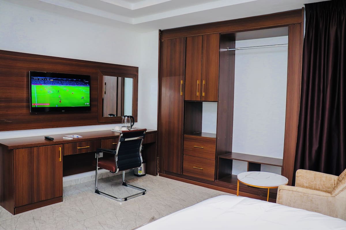Une chambre d’hôtel avec un bureau en bois, une télévision, un lit, une chaise et une armoire.