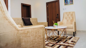 A living room with two beige sofas, a round coffee table with a patterned rug, and a painting on the wall. - Grand Palmac Hotel (Abuja)