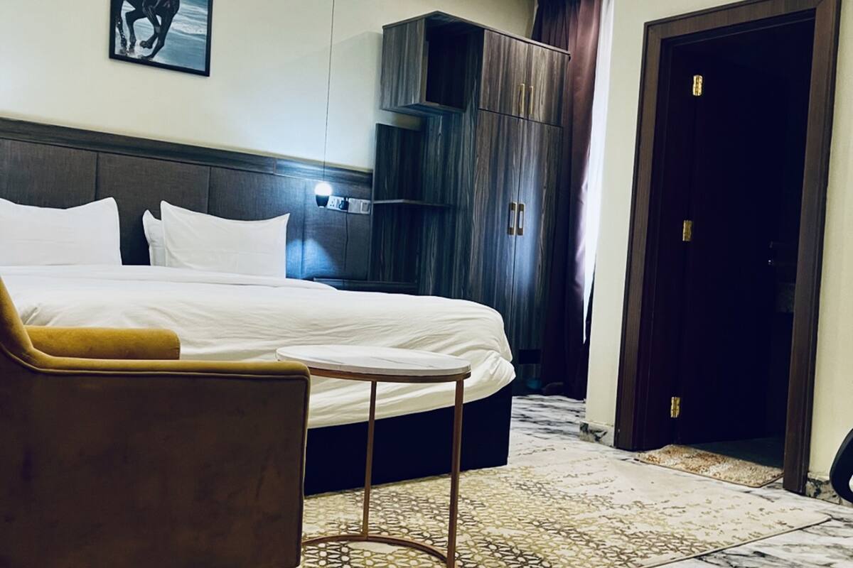 Une chambre d’hôtel avec un lit, une petite table ronde, un canapé, une armoire et une porte.