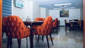 A dining area with orange upholstered chairs, a wooden table, and a painting on the wall. - Grand Palmac Hotel (Abuja)