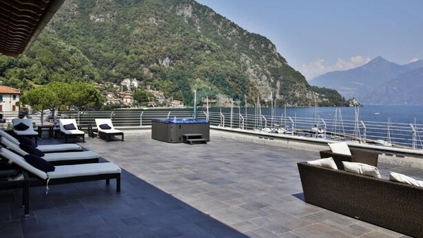 A terrace with sun loungers and a view of a mountainous coastline.