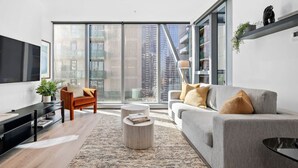 A modern living room with a large window, a grey sofa, a wooden coffee table, and a black TV stand.