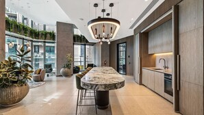 A modern kitchen with a marble island, pendant lighting, and a view of greenery through large windows.