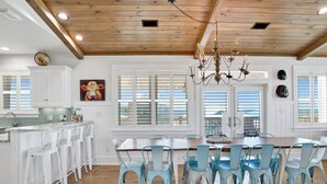 Een ruime keuken met een houten plafond, witte keukenkastjes en een groot kookeiland met barkrukken.