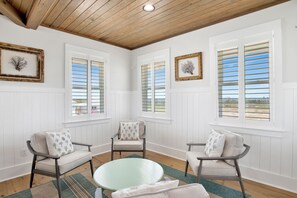 A room with white paneled walls, a wooden ceiling, and three chairs with cushions. There are two windows with shutters, and a framed picture on the wall. - Coastal Retreat | Private Heated Pool | Elevator and Beach Access (Gulf Shores)
