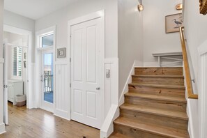 A staircase with wooden steps and white walls, leading to a landing with a framed picture. - Coastal Retreat | Private Heated Pool | Elevator and Beach Access (Gulf Shores)