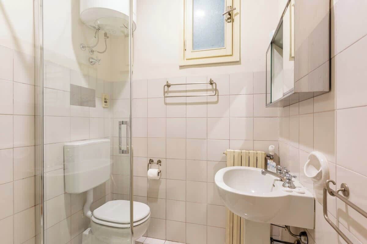 A bathroom with a toilet, a sink, a glass shower enclosure, and a towel rack.