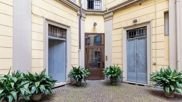 A courtyard with a cobblestone floor, two potted plants, and a central door with a window above it. - Tricolore · (Piazza Tricolore) Metro Blu Duomo a 10 minuti (Milano)
