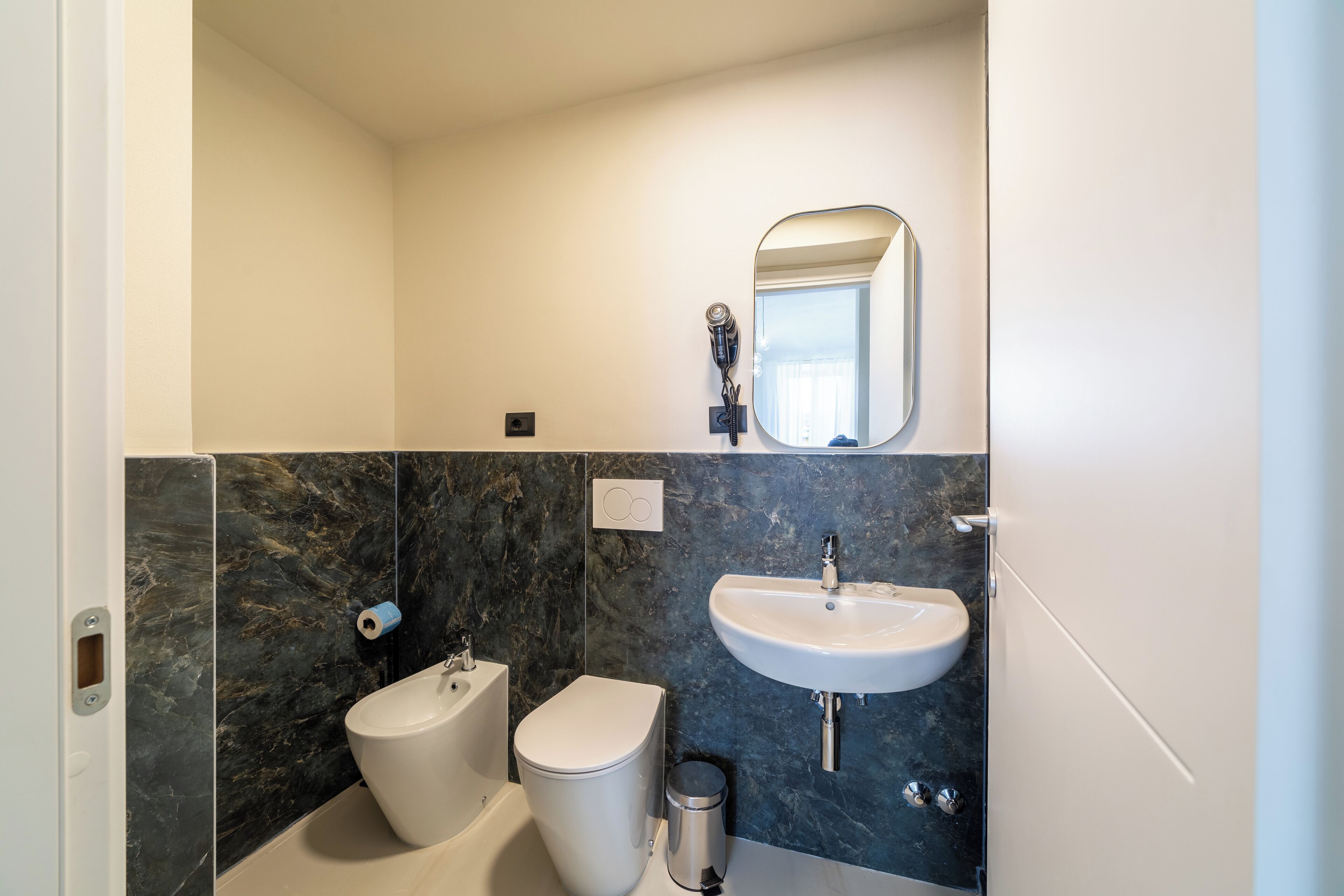 A modern bathroom with a bidet, toilet, sink, and mirror.