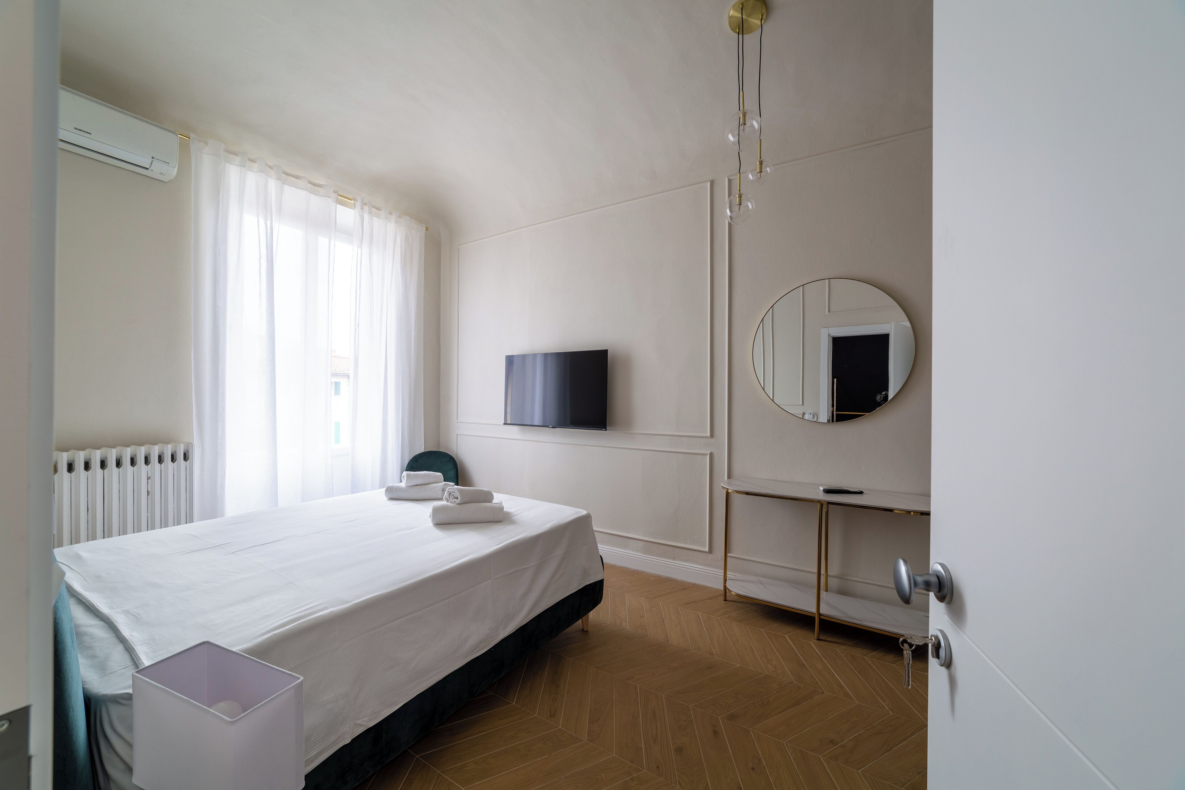A hotel room with a bed, a TV, a mirror, and a radiator.