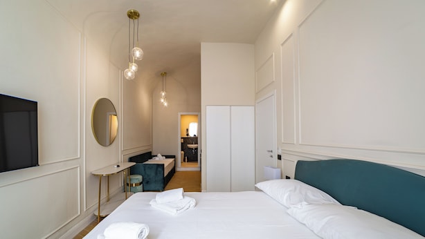 Habitación de hotel con una cama grande, un escritorio, una silla, un televisor, un espejo y un armario.