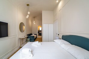 A hotel room with a large bed, a desk, a chair, a TV, a mirror, and a wardrobe. - Residenza d'Epoca White Room (Florence)
