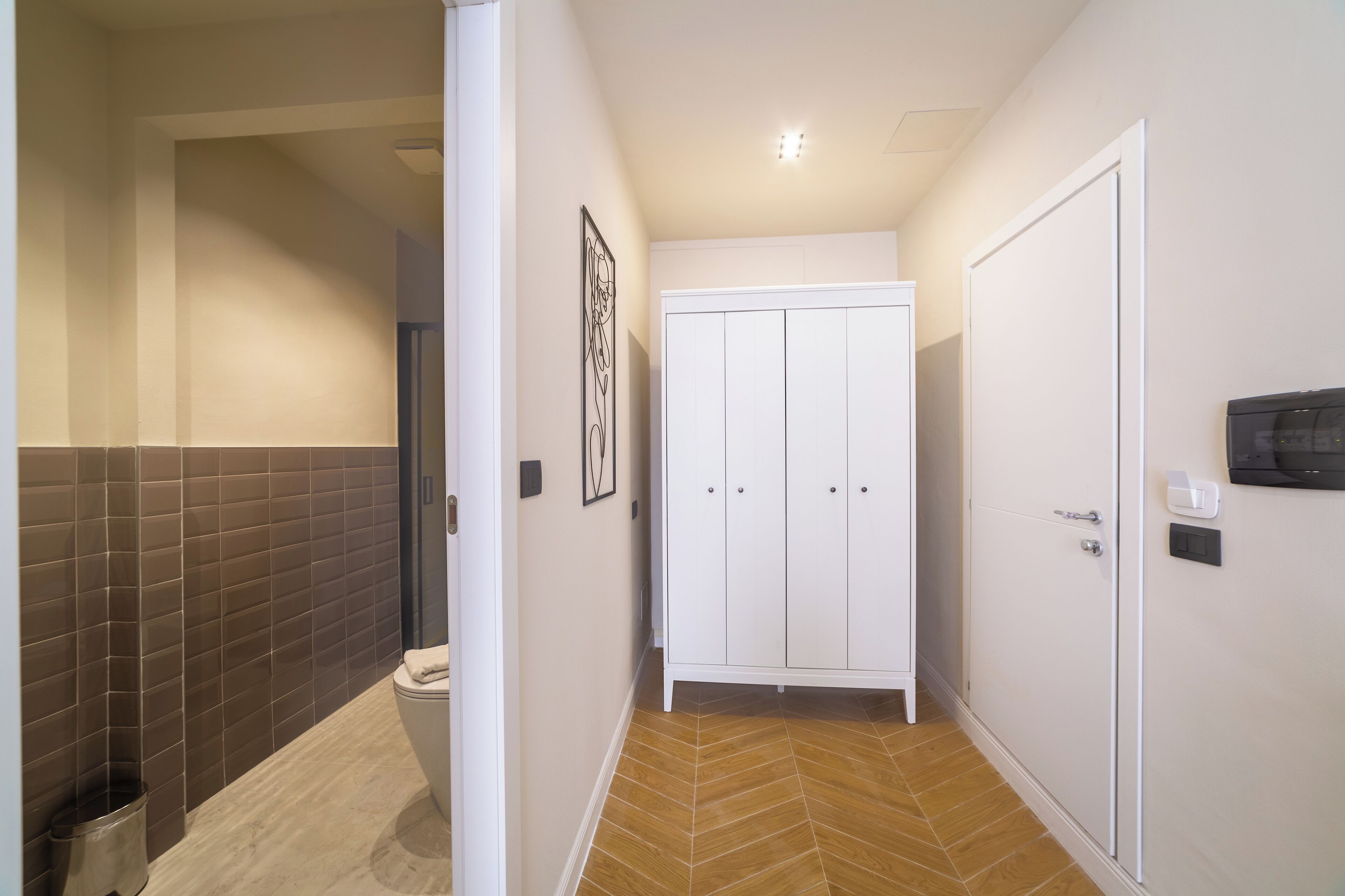A narrow hallway with a toilet, a white wardrobe, and a tiled wall.