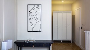 Un pasillo con una obra de arte abstracta en marco negro, una consola de madera oscura con revistas y un armario blanco.