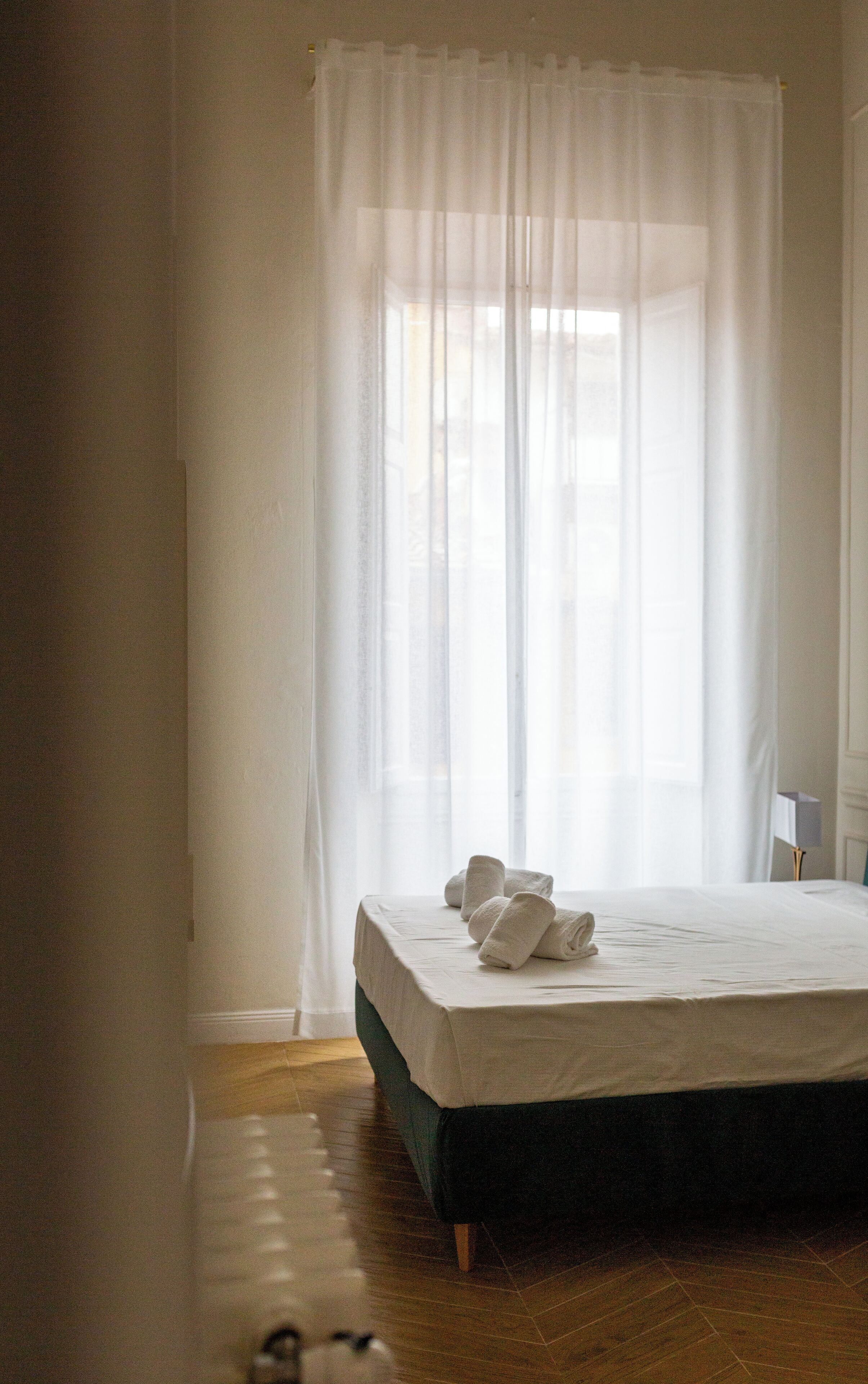 A bedroom with a bed, white curtains, and a wooden floor.