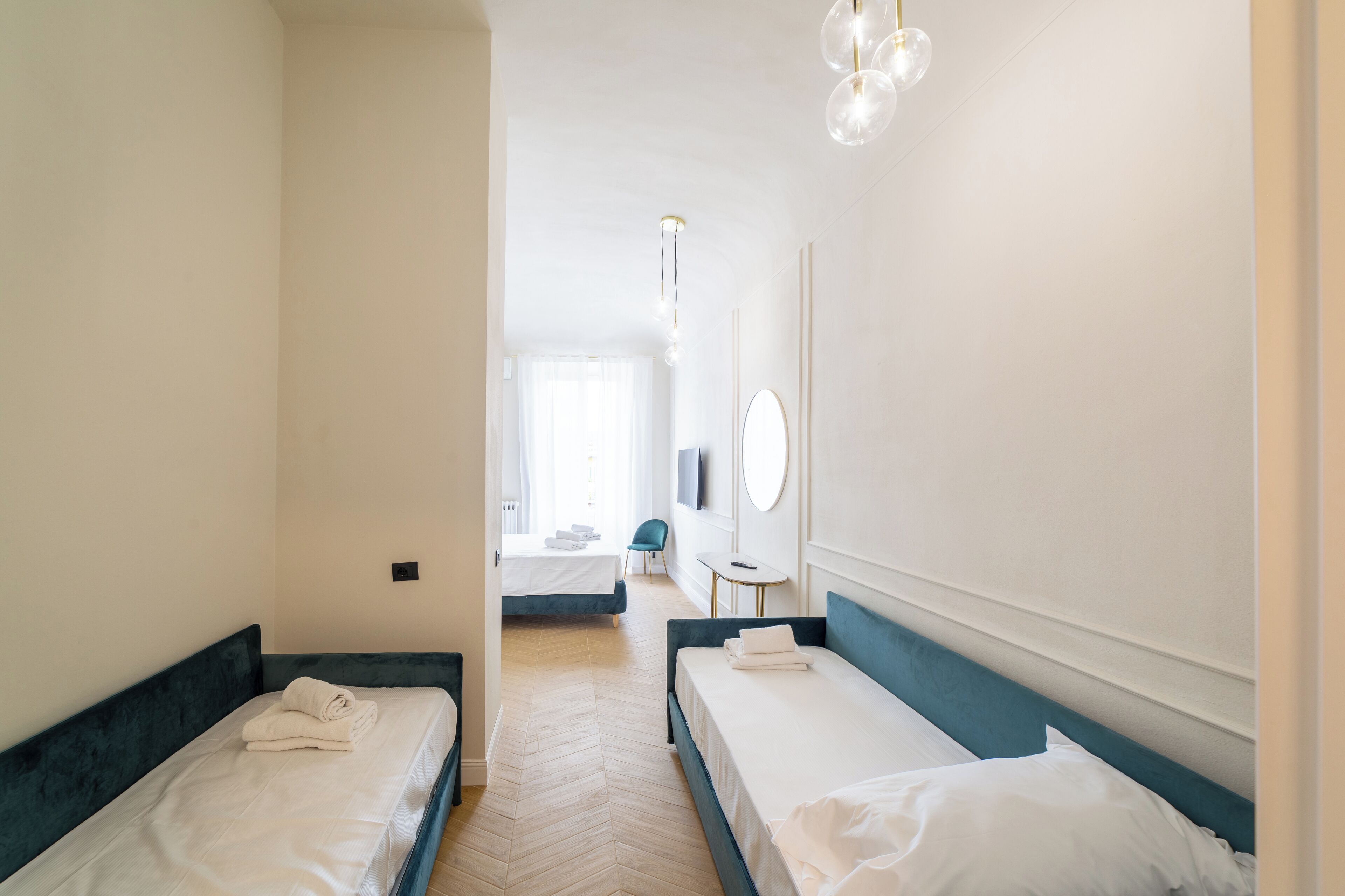 A hotel room with two single beds, a small table, a chair, and a TV on the wall.