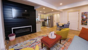 Un salon moderne avec une cheminée, un coin repas avec une table et des chaises, et une cuisine en arrière-plan.