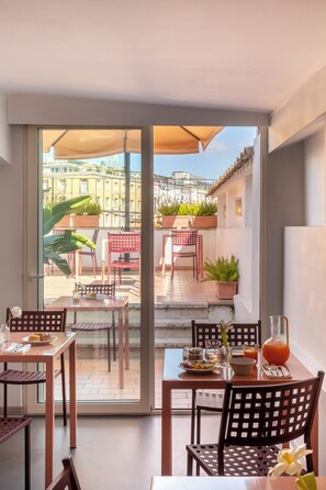 Un espace repas avec des tables et des chaises, une porte vitrée donnant sur l’extérieur et des plantes en pot.