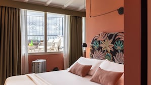 Une chambre d’hôtel avec un lit, des rideaux, une fenêtre donnant sur un balcon et une tête de lit à motifs.