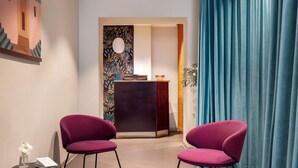Un espace d’accueil comprenant un bureau, deux chaises, un vase avec une fleur et un mur orné d’un motif floral.